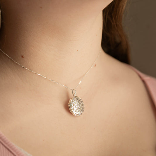 Silver locket necklace with a textured pendant on a person wearing a pink top.