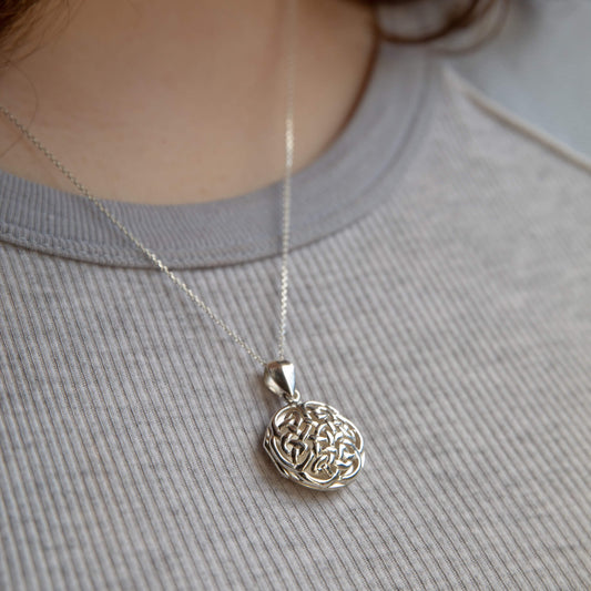 Large silver locket with celtic design worn by model wearing grey shirt