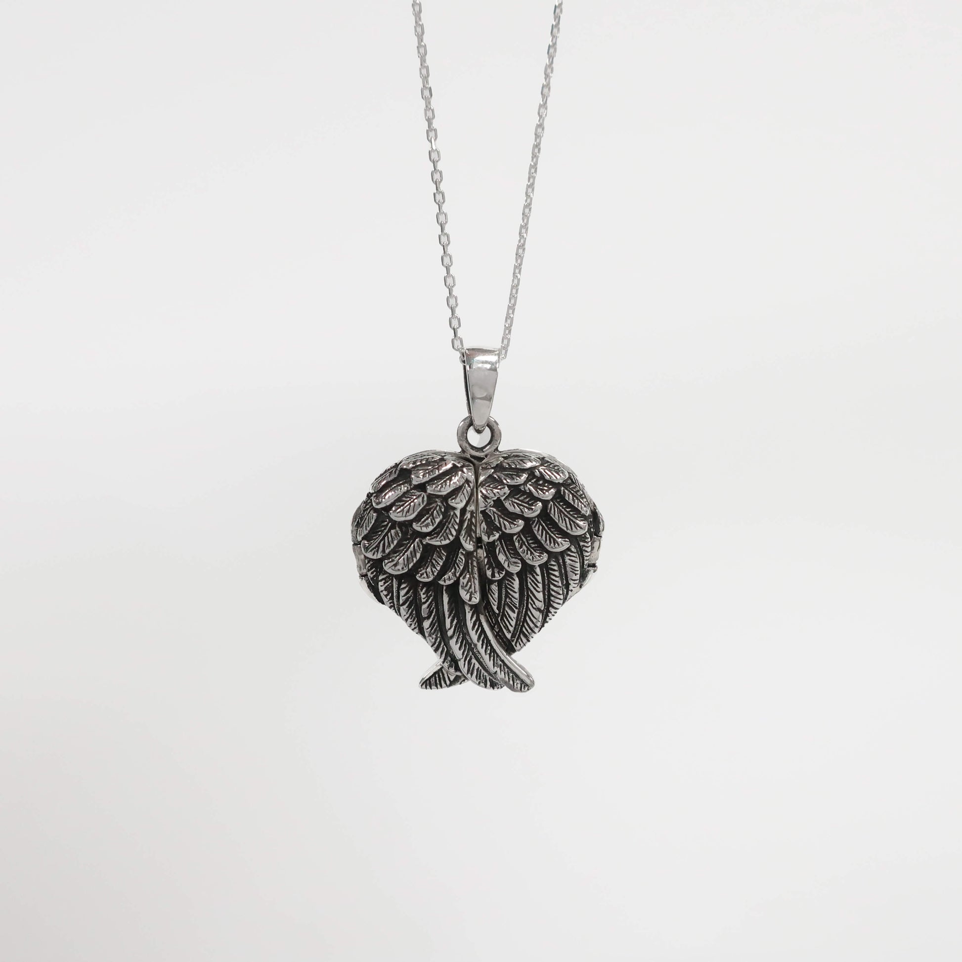 Silver angel wing pendant on a chain against a light gray background