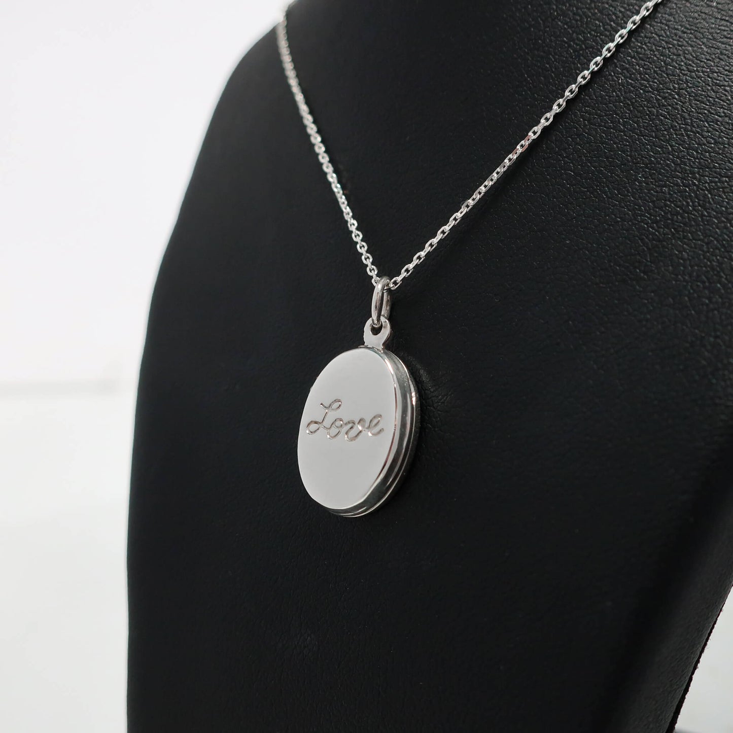 Silver necklace with an oval locket engraved with 'Love' on a black mannequin.