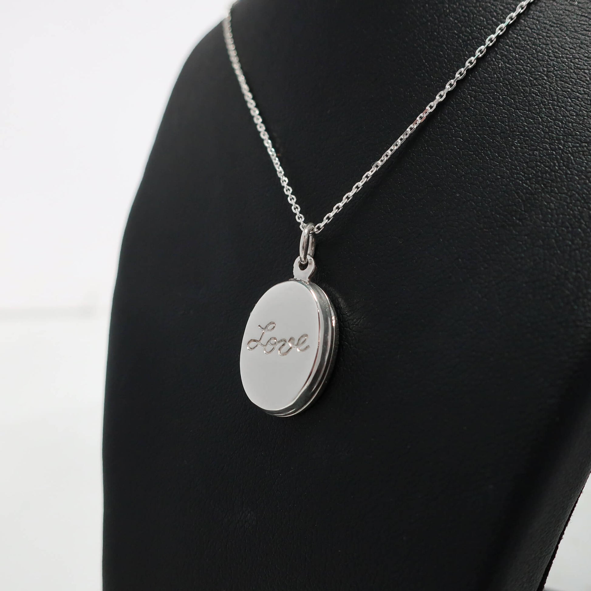 Silver necklace with an oval locket engraved with 'Love' on a black mannequin.