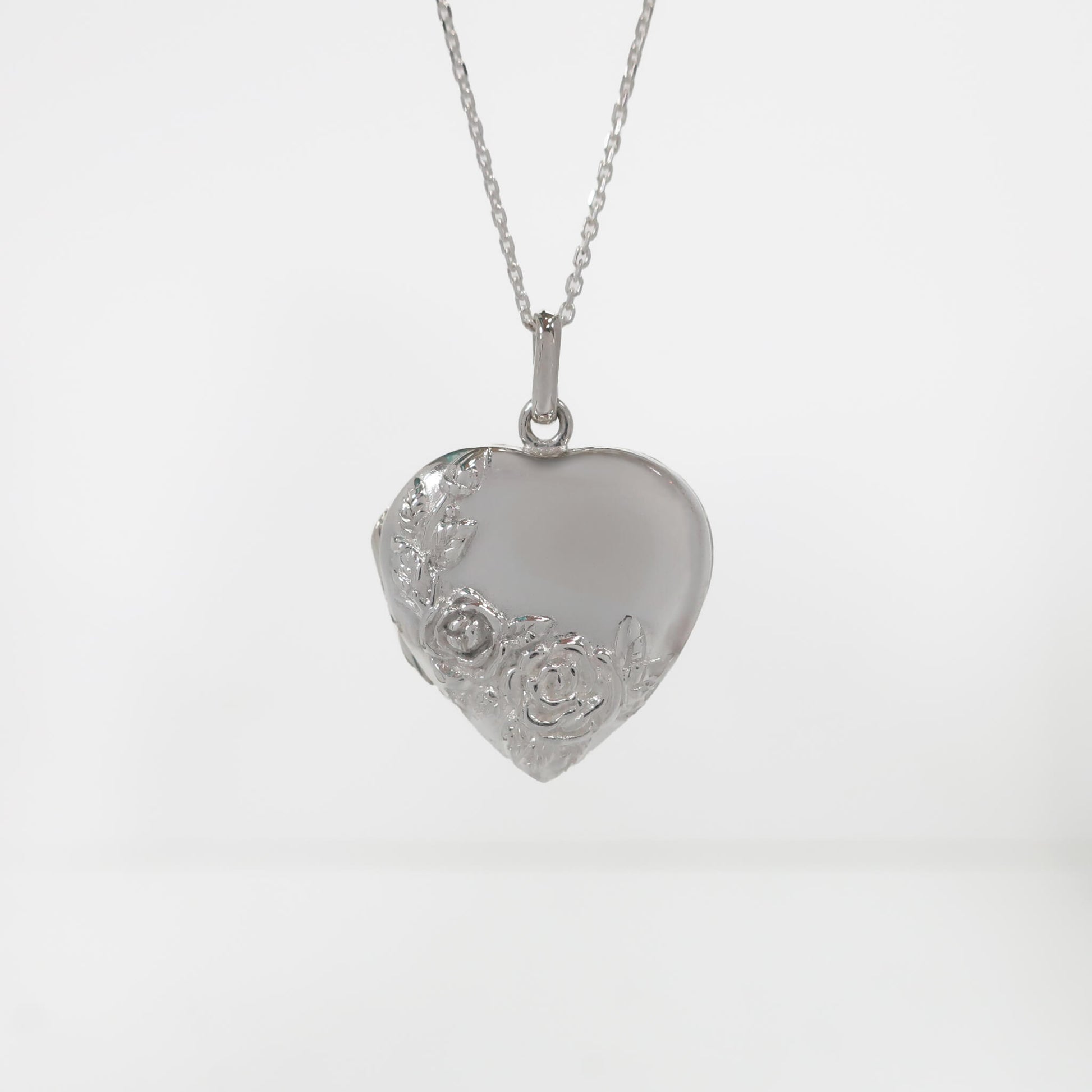 Silver heart-shaped pendant with floral designs on a white background