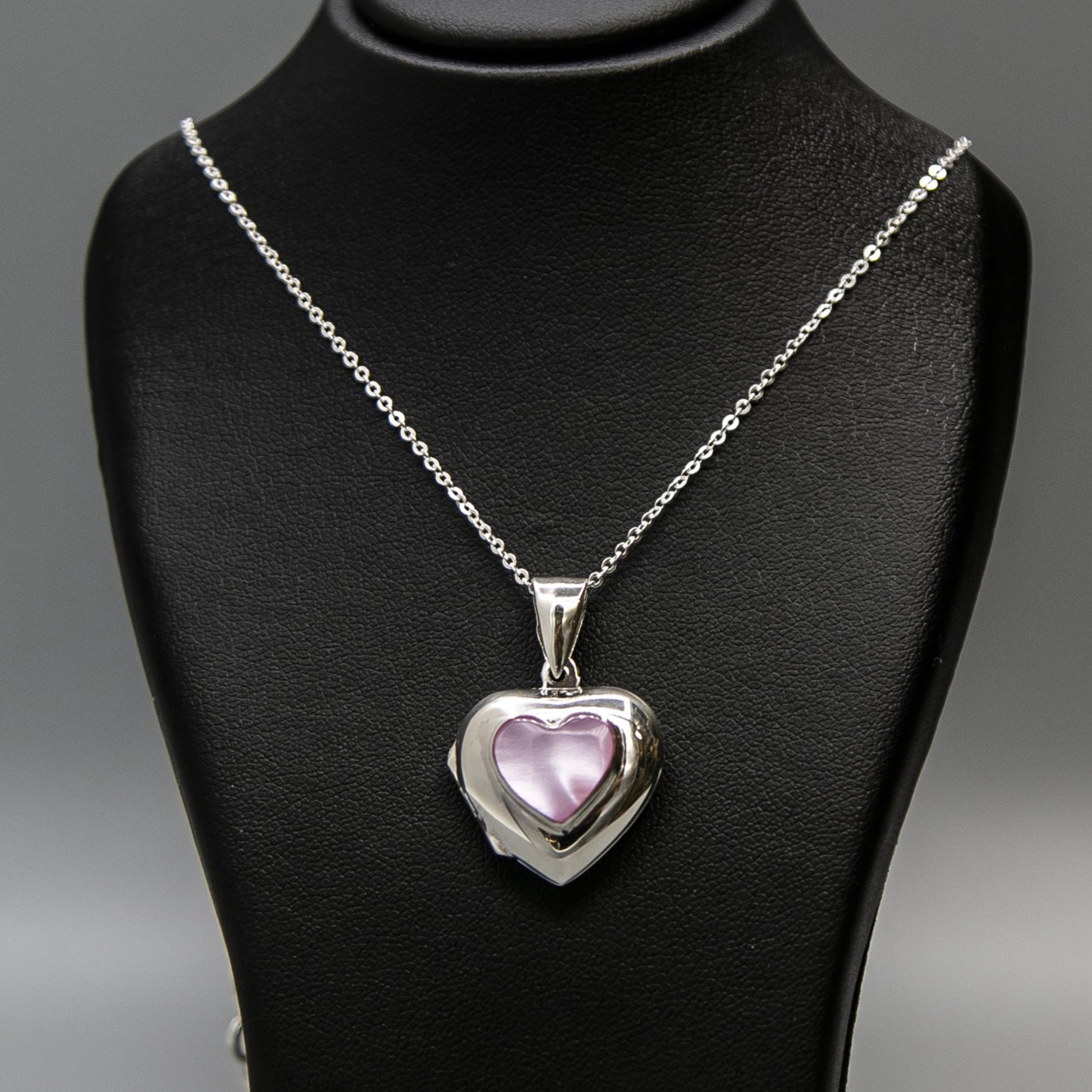 Silver heart-shaped photo locket necklace  with pink mother of pearl inset with a silver Italian chain displayed on a black bust.