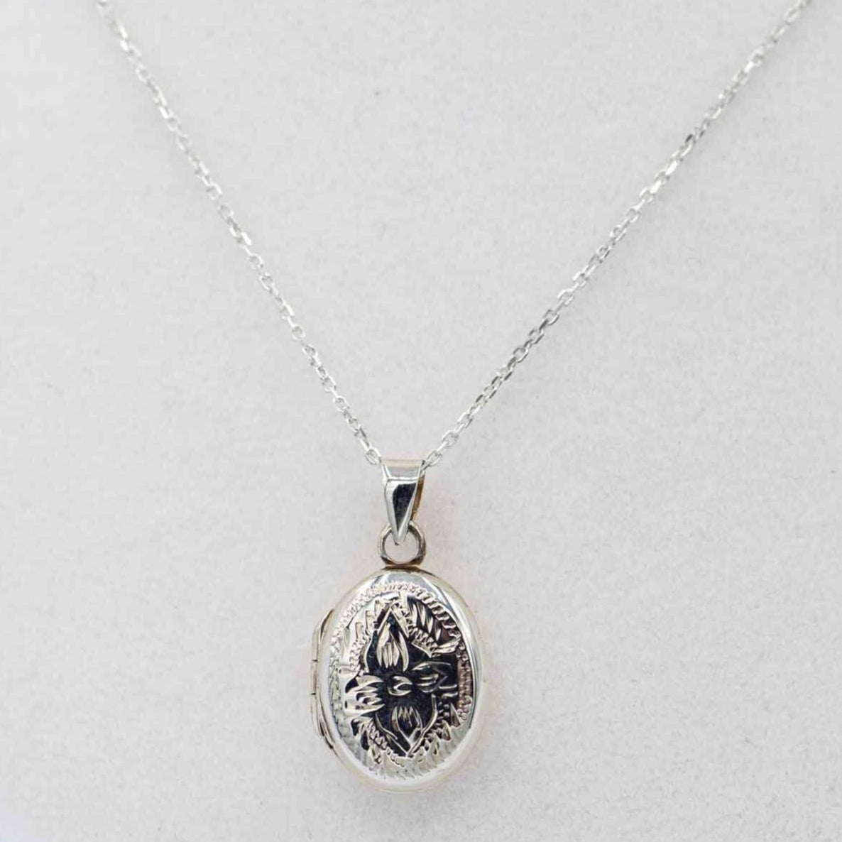 dainty ornate oval silver locket on white bust.
